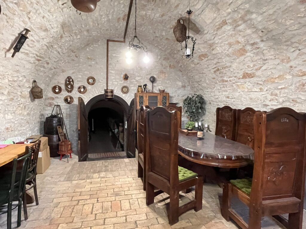 Inside an old Hungarian wine cellar with wooden table and chairs, and stone walls.