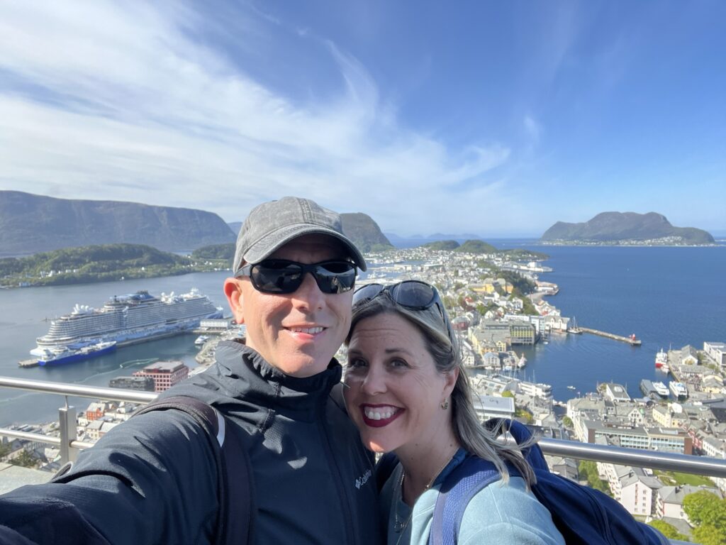 two people taking a selfie on top of mountain in alesund with cruise ship in background